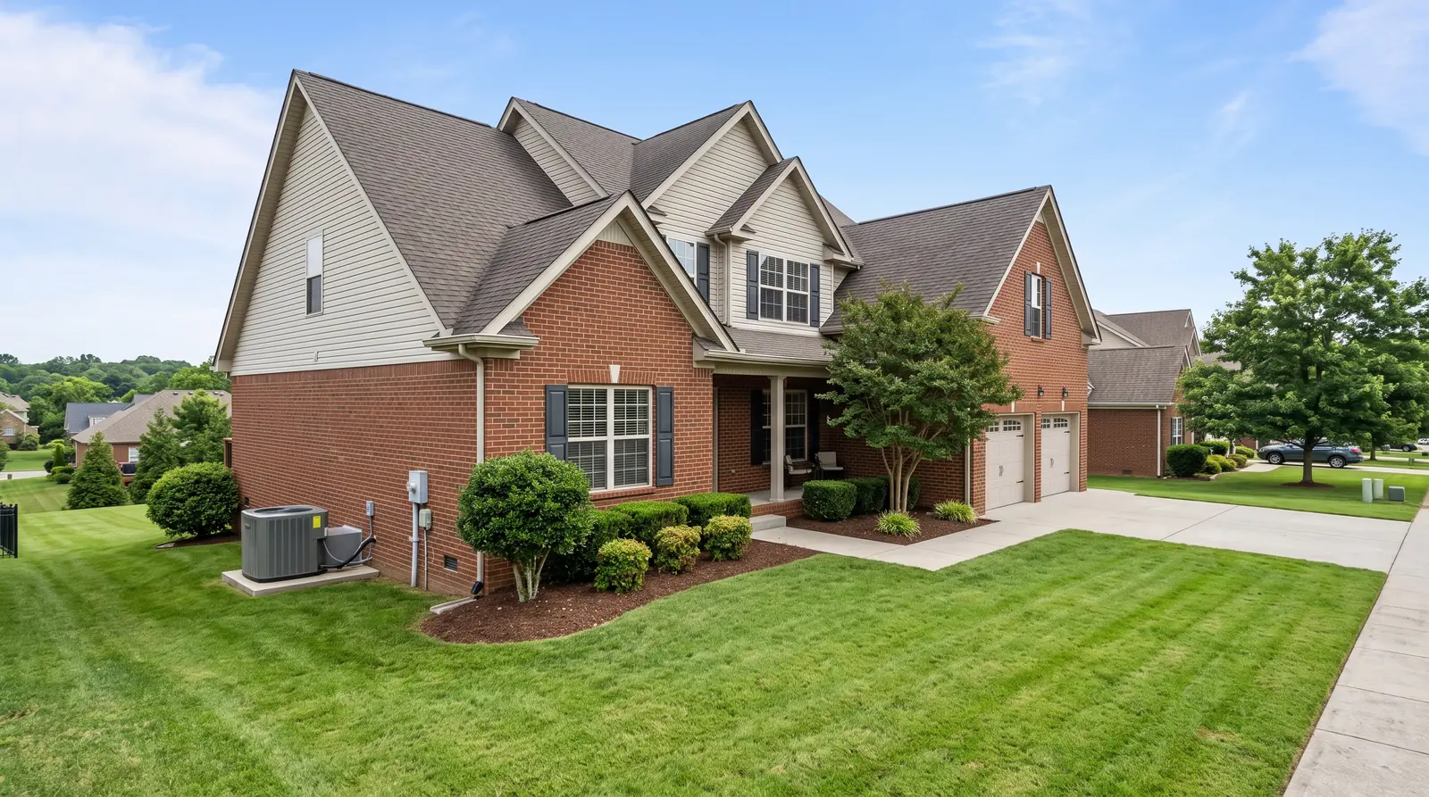 A well-kept two-story suburban Middle Tennessee home with a two-car garage and a tidy lawn under a blue sky, an outdoor condenser on a pad beside the side wall