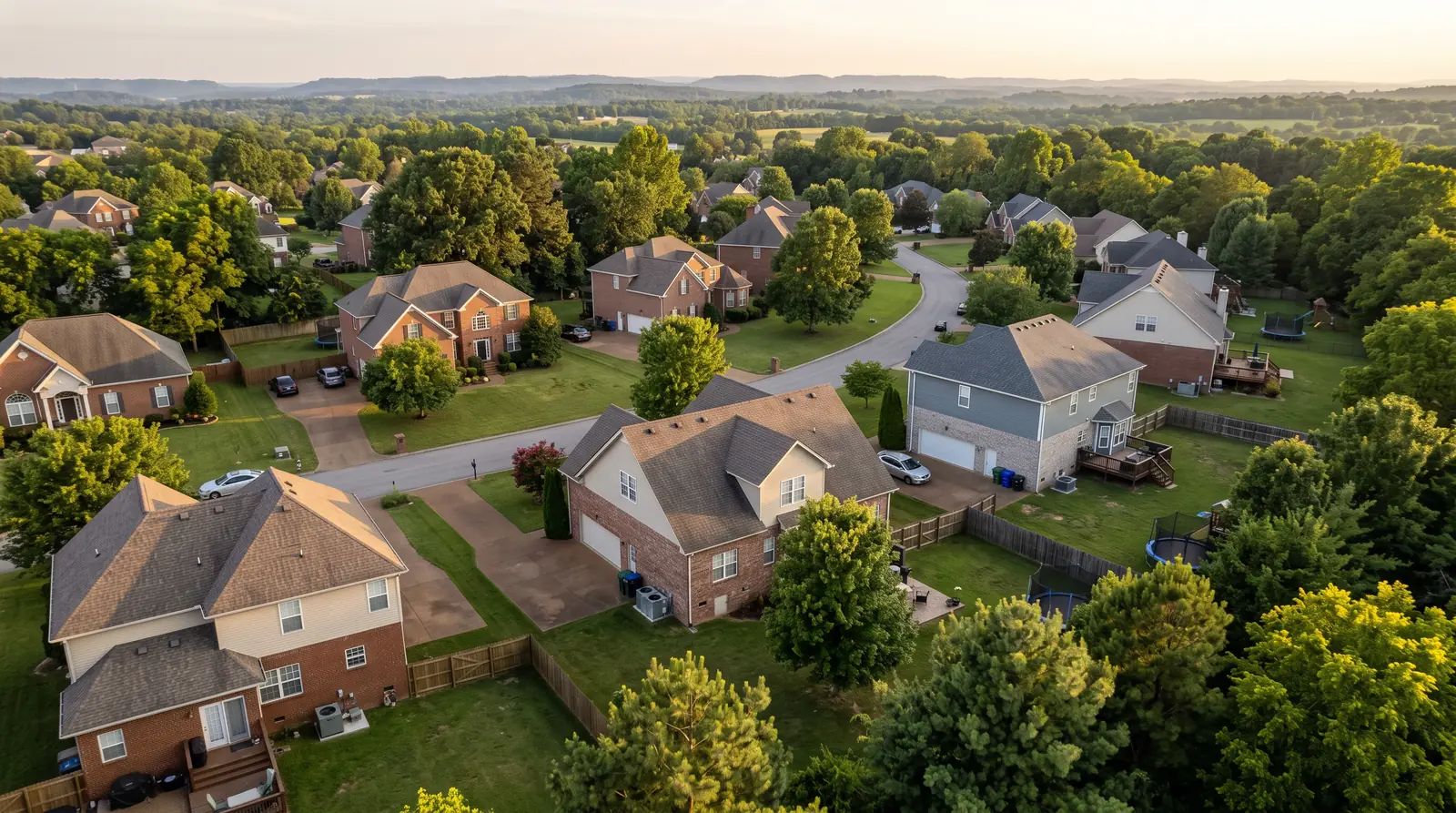 Aerial View of Middle Tennessee Neighborhoods | Music City HVAC An aerial view over a green Middle Tennessee neighborhood at golden hour showing brick and siding homes, mature trees, rolling hills in the distance and a few outdoor condensers visible beside the houses