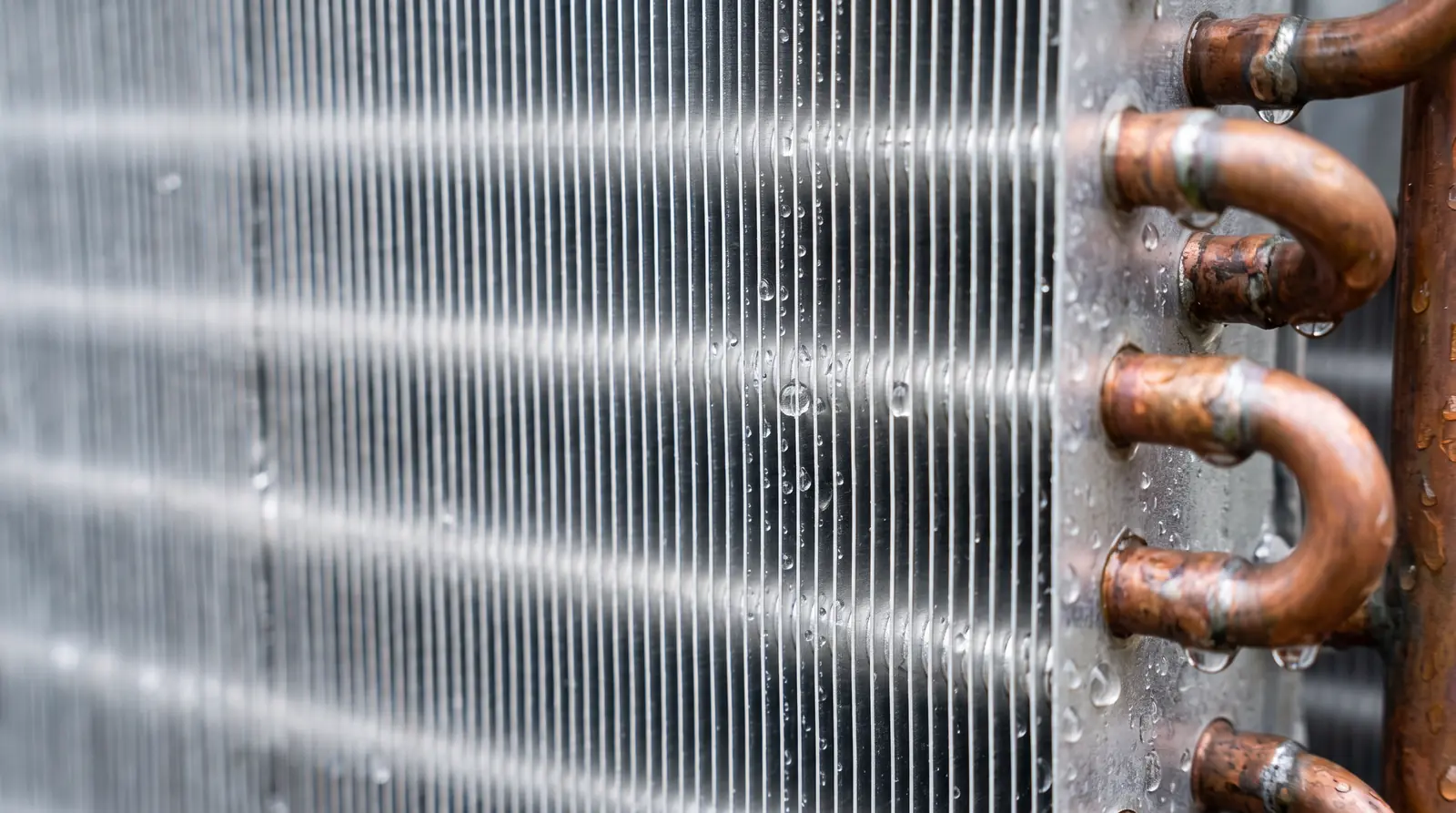 A macro close-up of clean aluminum condenser coil fins glistening with water droplets after rinsing, evenly spaced fins and copper tube ends, soft daylight, shallow depth of field